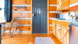 Interno di una baita di legno con una porta in legno scuro, pensili in legno, un forno a microonde e un lavello.