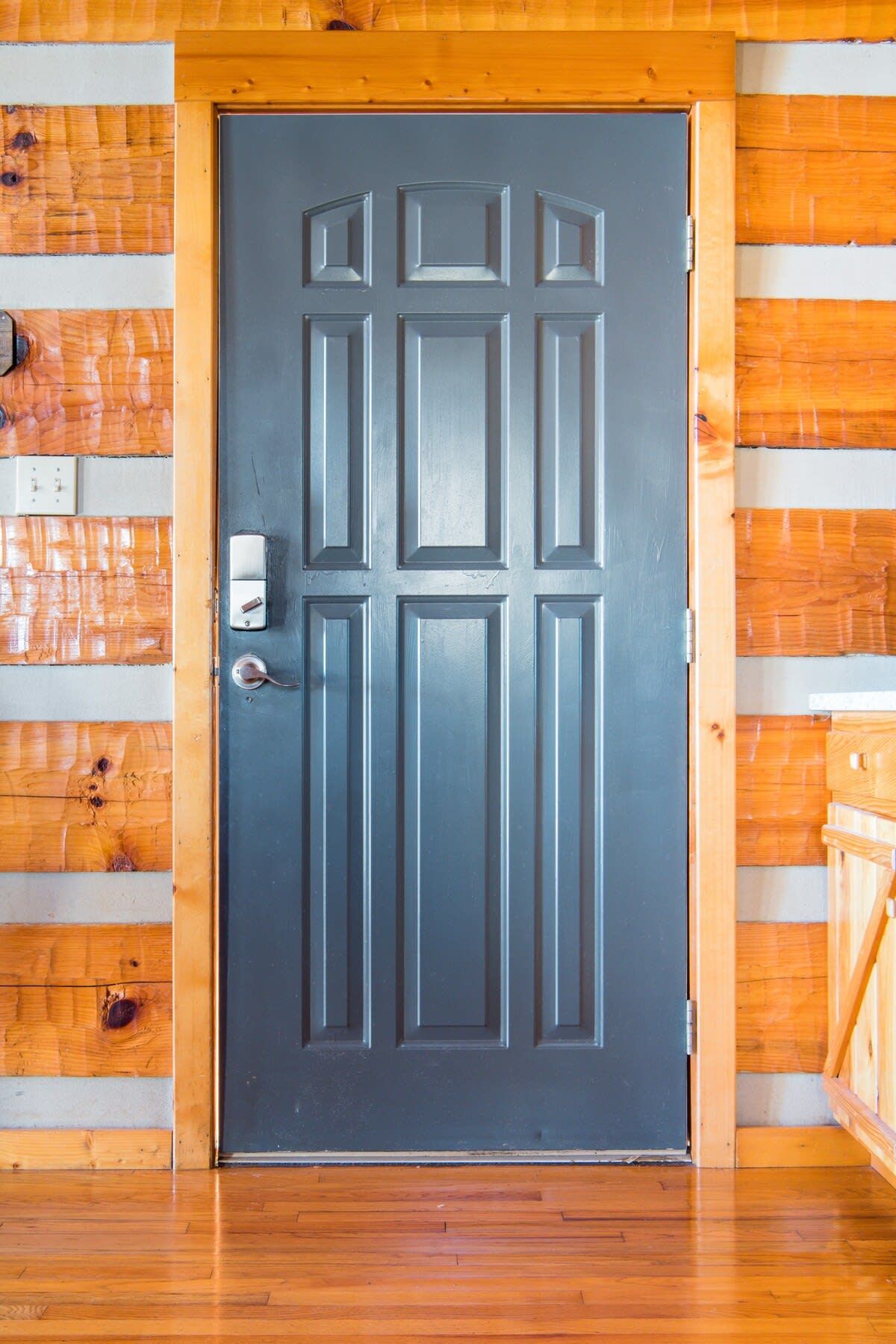 Puerta gris con manija plateada y cerradura, en un muro de madera con tablones horizontales.