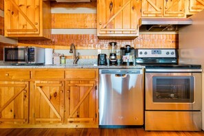 Una cocina con armarios de madera, electrodomésticos de acero inoxidable, incluyendo lavavajillas, microondas, cafetera y estufa.