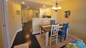 Un comedor con una mesa de madera y sillas azules, una cocina al fondo y un pasillo que conduce a otras habitaciones.