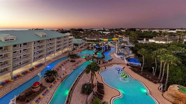 Un hotel con múltiples piscinas, un parque acuático y vista al océano al atardecer.