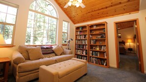 Una camera accogliente con soffitto in legno, ampie finestre, un divano, una libreria e un telescopio.