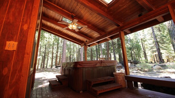 Una baita in legno con idromassaggio, terrazza in legno e vista sulla foresta.