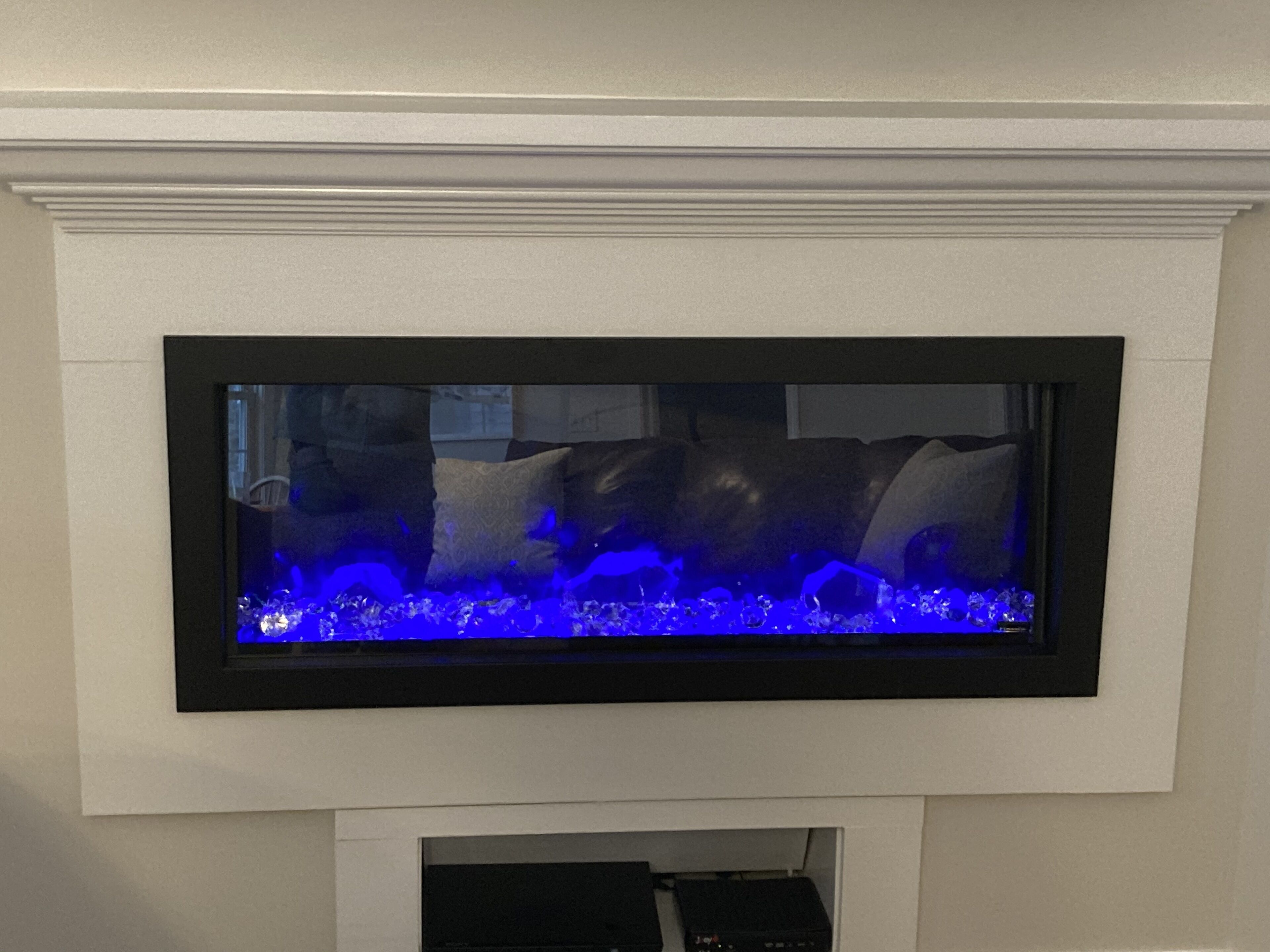 Ein rechteckiges Aquarium mit schwarzem Rahmen, platziert an einer weißen Wand über einem Kamin.