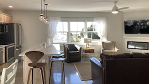 A modern kitchen with a central island, bar stools, a dining table, and a seating area with a sofa and chairs. - Charming Carriage House - Beach - Ocean Views - Fireplace (New London)