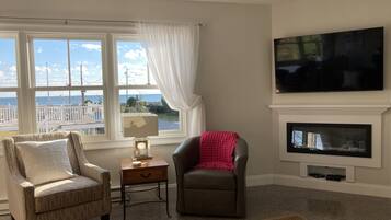 A living room with a view of the ocean, a fireplace, a television, and two chairs.