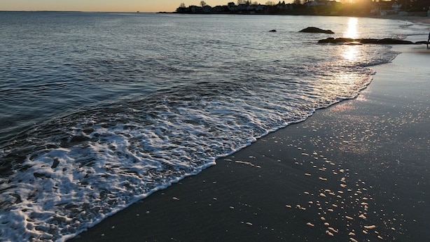 A beach with waves gently lapping onto the shore, a clear sky, and the sun setting in the distance. - Charming Carriage House - Beach - Ocean Views - Fireplace (New London)