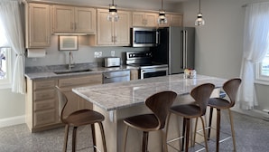 A modern kitchen with wooden cabinets, a central island with bar stools, stainless steel appliances, and pendant lighting. - Charming Carriage House - Beach - Ocean Views - Fireplace (New London)