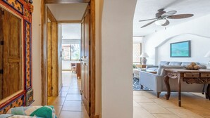 Un couloir mène à un espace de vie comprenant un ventilateur de plafond, un canapé et une table sur laquelle est posé un vase décoratif.