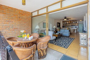 Un patio con una mesa y sillas, un muro de ladrillo y vista a una sala de estar con sofá y ventilador de techo.