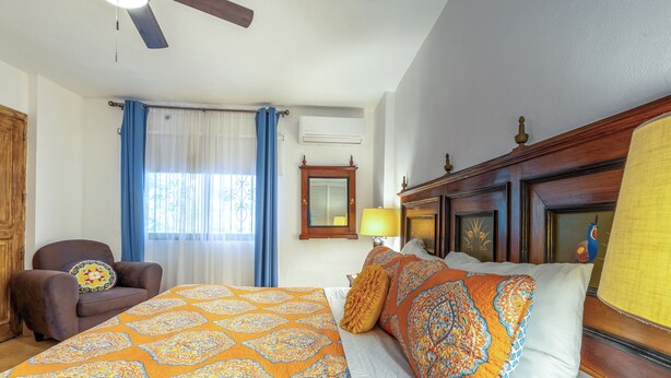 Une chambre d’hôtel comprenant un lit, une chaise, une fenêtre avec des rideaux, un ventilateur de plafond et un climatiseur fixé au mur.