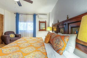 A hotel room with a bed, a chair, a window with curtains, a ceiling fan, and a wall-mounted air conditioner.