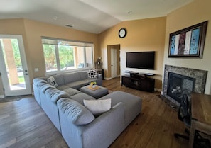 A living room with a gray sectional sofa, a flat-screen TV, a fireplace, and a large window.