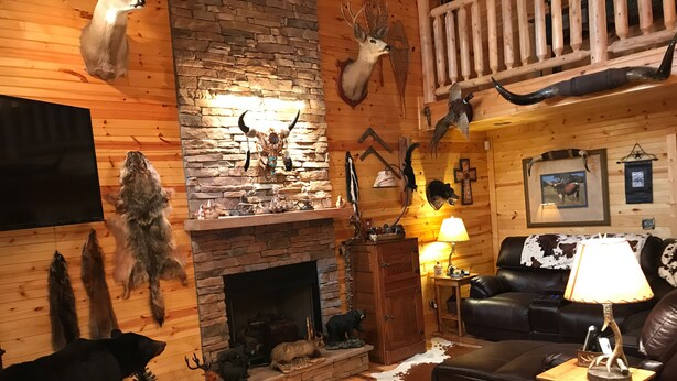 A rustic living room with a stone fireplace, mounted animal heads, and a leather couch.