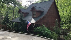A wooden cabin with a steep roof, surrounded by dense forest.