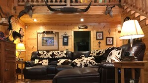 A log cabin interior with a leather sofa, wooden walls, and various hunting trophies.