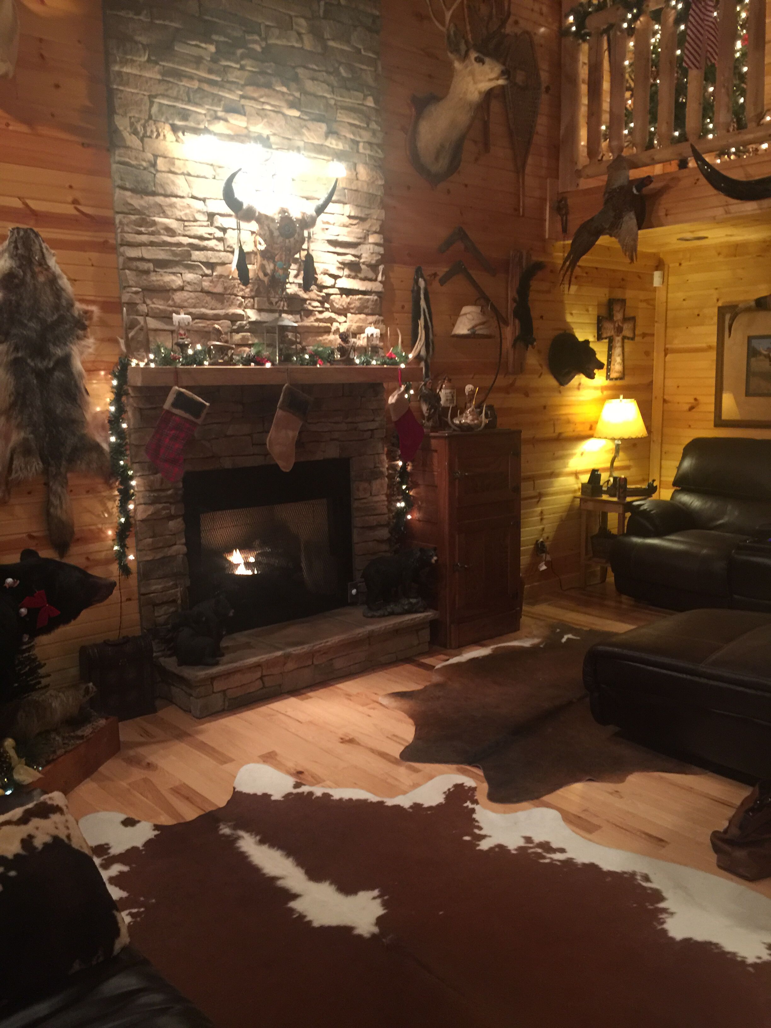 Ein gemütliches Wohnzimmer mit Kamin aus Stein, einer Ledersofa und verschiedenen Jagdtrophäen an den Wänden.