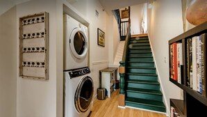 A laundry room with a washing machine and dryer, a staircase with green steps, and a bookshelf with books. - 1880 Victorian In Heart Of Downtown  (St. Augustine)