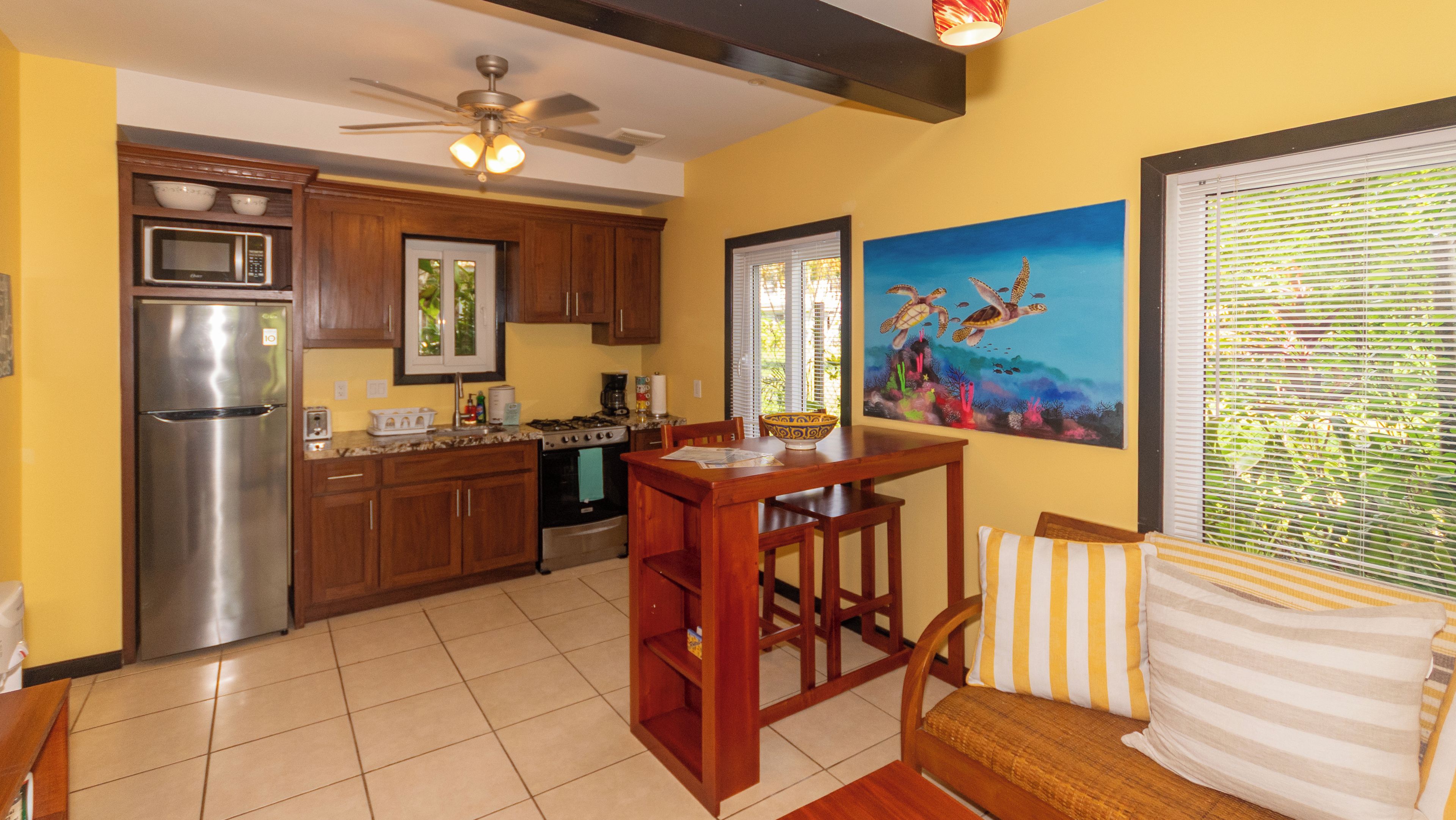 A kitchen with wooden cabinets, a stainless steel refrigerator, a dining table with chairs, and a painting of sea turtles on the wall.