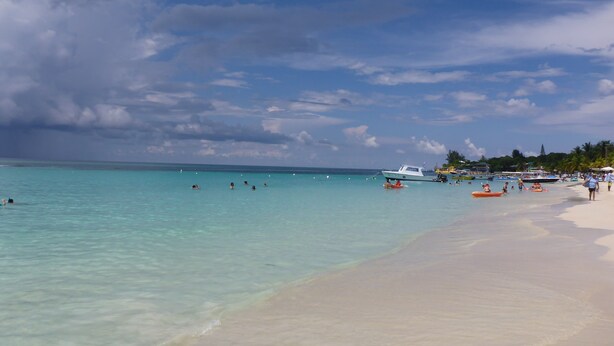 Een strand met helder turquoise water, een zandstrand en enkele boten.
