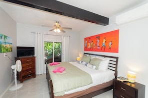 A bedroom with a bed, a ceiling fan, a TV, a dresser, and a painting on the wall.