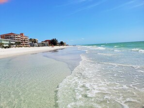 A beach with clear water, a sandy shore, and buildings in the background. - BEACH & POOL! LUXURY MODERN FLORIDA VACATION HOME @ BAREFOOT BEACH RESORT!  (Indian Shores)