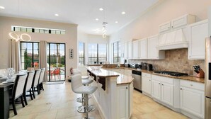 A modern kitchen with white cabinetry, a central island, and a dining area with bar stools. - Spacious, game room, golf view, private pool & BBQ (Kissimmee)