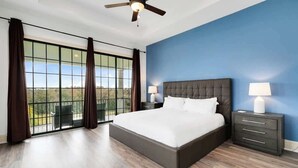 A bedroom with a large bed, a ceiling fan, a nightstand with a lamp, and a view through large windows. - Spacious, game room, golf view, private pool & BBQ (Kissimmee)