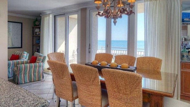 En matplats med flätade stolar och en kristallkrona, en randig soffa och utsikt över havet.