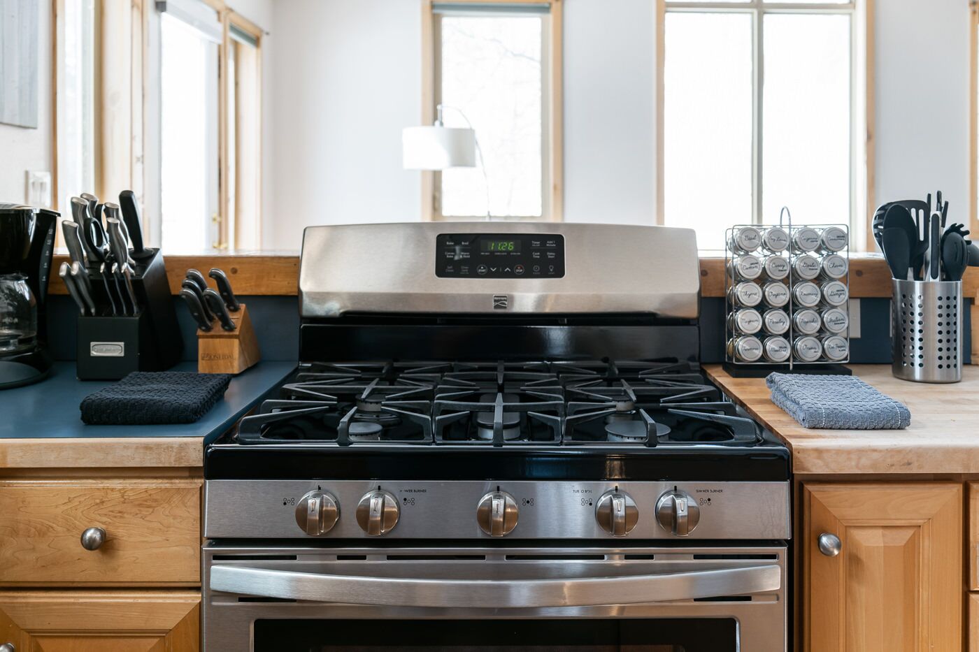 A kitchen with a stainless steel stove, a digital clock, and various kitchen utensils.