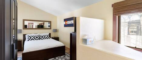 A bedroom with a bed, a bedside table, a lamp, a mirror, a window with a view, and a bedside box of tissues.