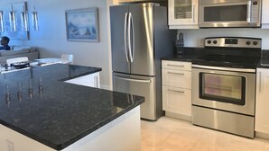 A modern kitchen with stainless steel appliances, a black granite countertop, and white cabinetry.