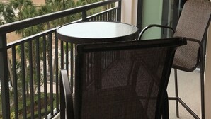 A balcony with a round table and two chairs, overlooking a beach and palm trees.
