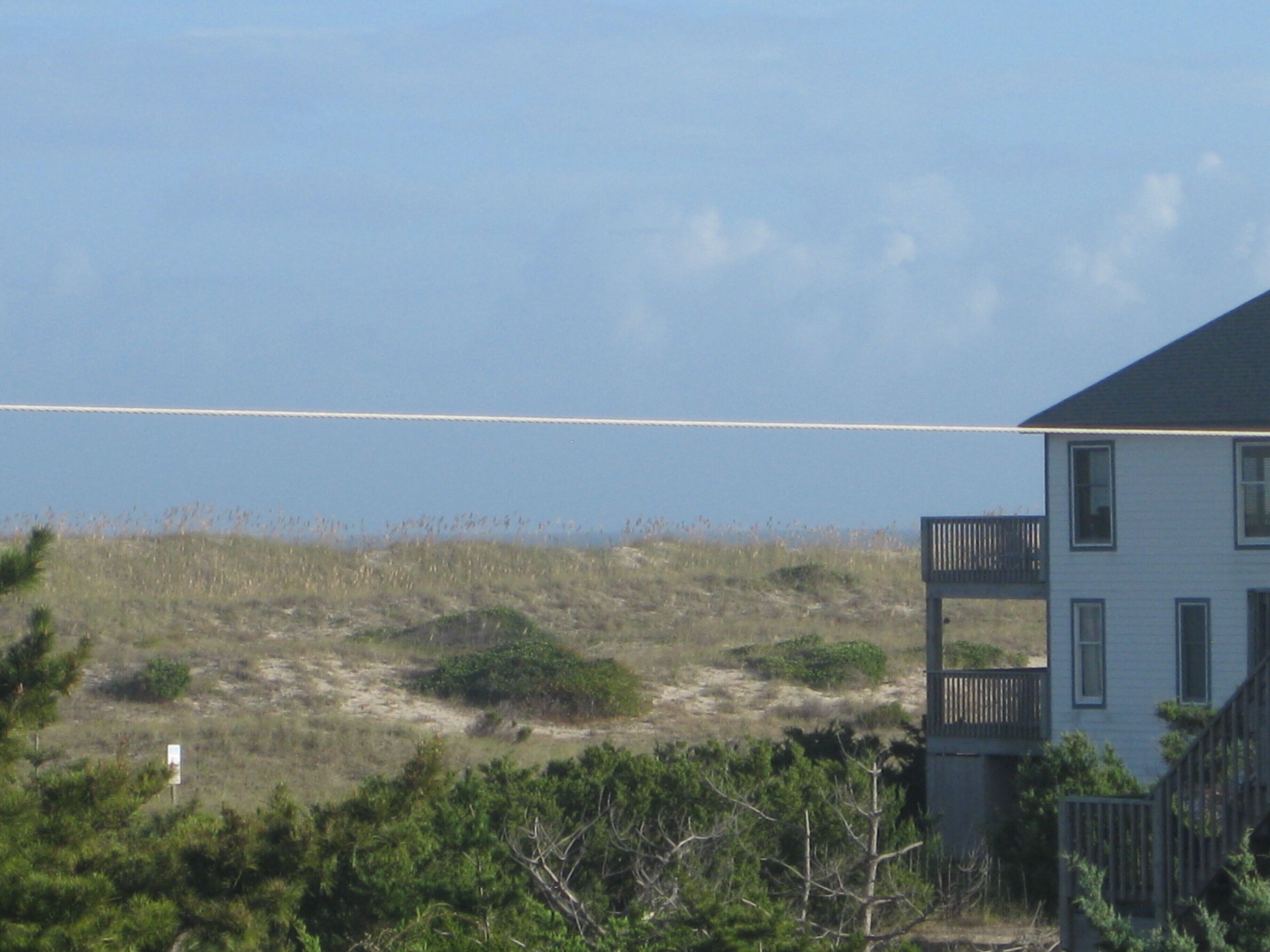 A house with a balcony, surrounded by vegetation and a clear sky.