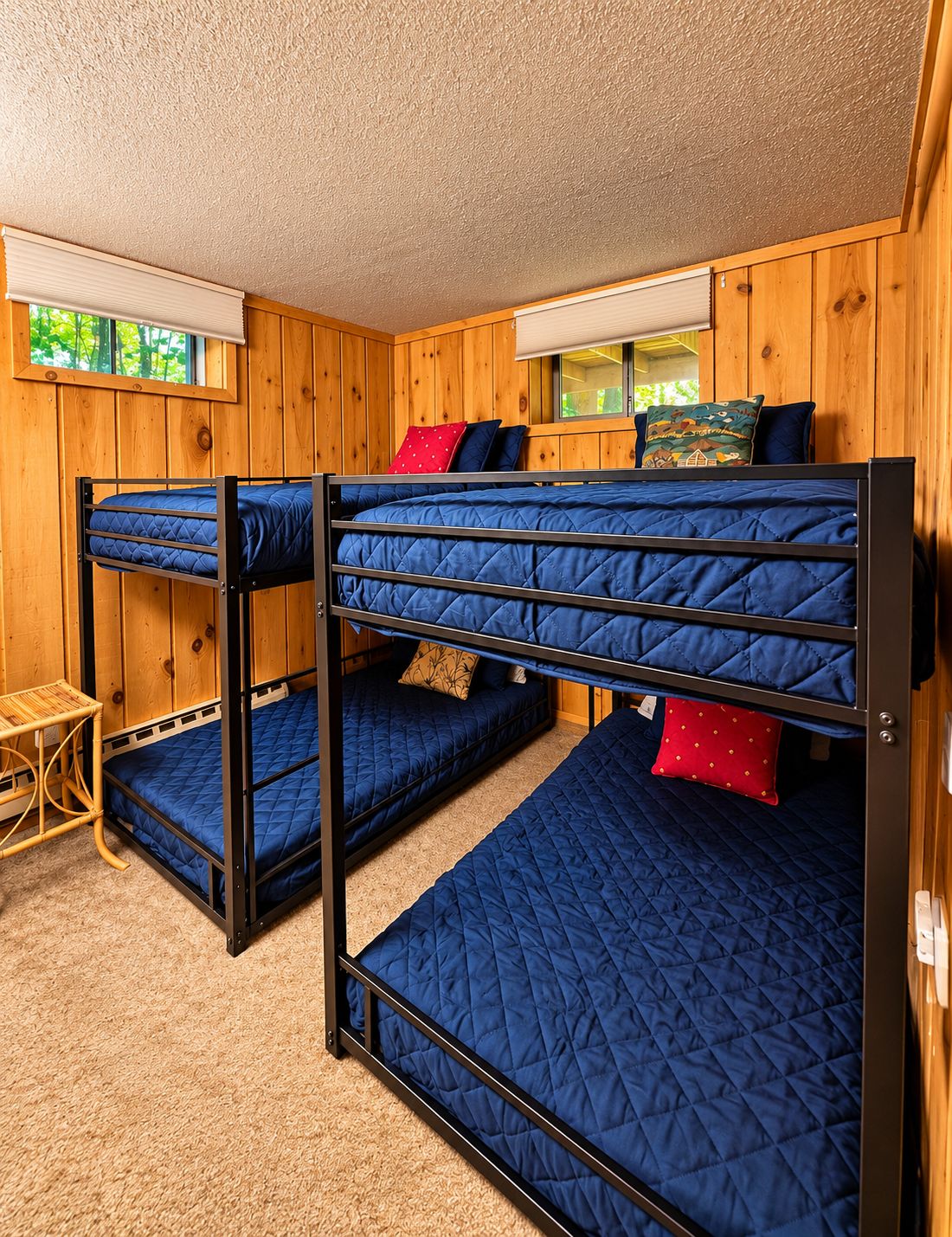 A bunk bed room with wooden walls, a small table, and a window with blinds.