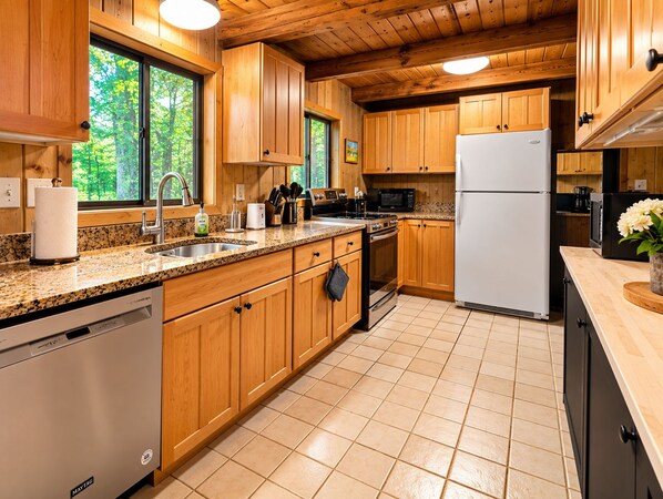 Una cocina moderna con armarios de madera, lavavajillas de acero inoxidable, refrigerador blanco y encimera de granito.