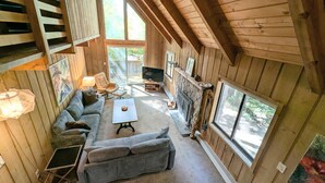 Ein gemütliches Blockhaus-Interieur mit Holzausbau, Kamin, Sofa, Couchtisch und großen Fenstern.