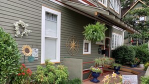 Une maison dotée d’un porche décoré de divers pots de plantes et de fleurs, d’une décoration en forme de boussole et d’une pancarte sur laquelle on peut lire : « Chez soi, on est bien ».
