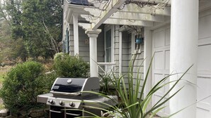 A barbecue grill in front of a house with a porch and a stone wall. - Guest Cottage on Country Estate (Watertown)