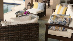 A covered outdoor seating area with wicker furniture, a pool, and a view of the water. - Waterfront Pool Home with Gulf Access (Cape Coral)