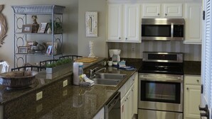 A kitchen with white cabinets, a granite countertop, stainless steel appliances, and a decorative shelf.