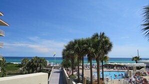 A resort pool area with palm trees, a clear blue sky, and a view of the ocean.