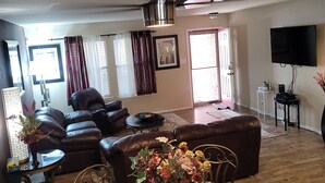 A spacious living room with a leather sofa, a glass coffee table with chairs, a ceiling fan, and a flat-screen TV mounted on the wall. - Air & Space Force Basic Training Grads/Ex-Large home mins from Lackland AFB/Golf (San Antonio)
