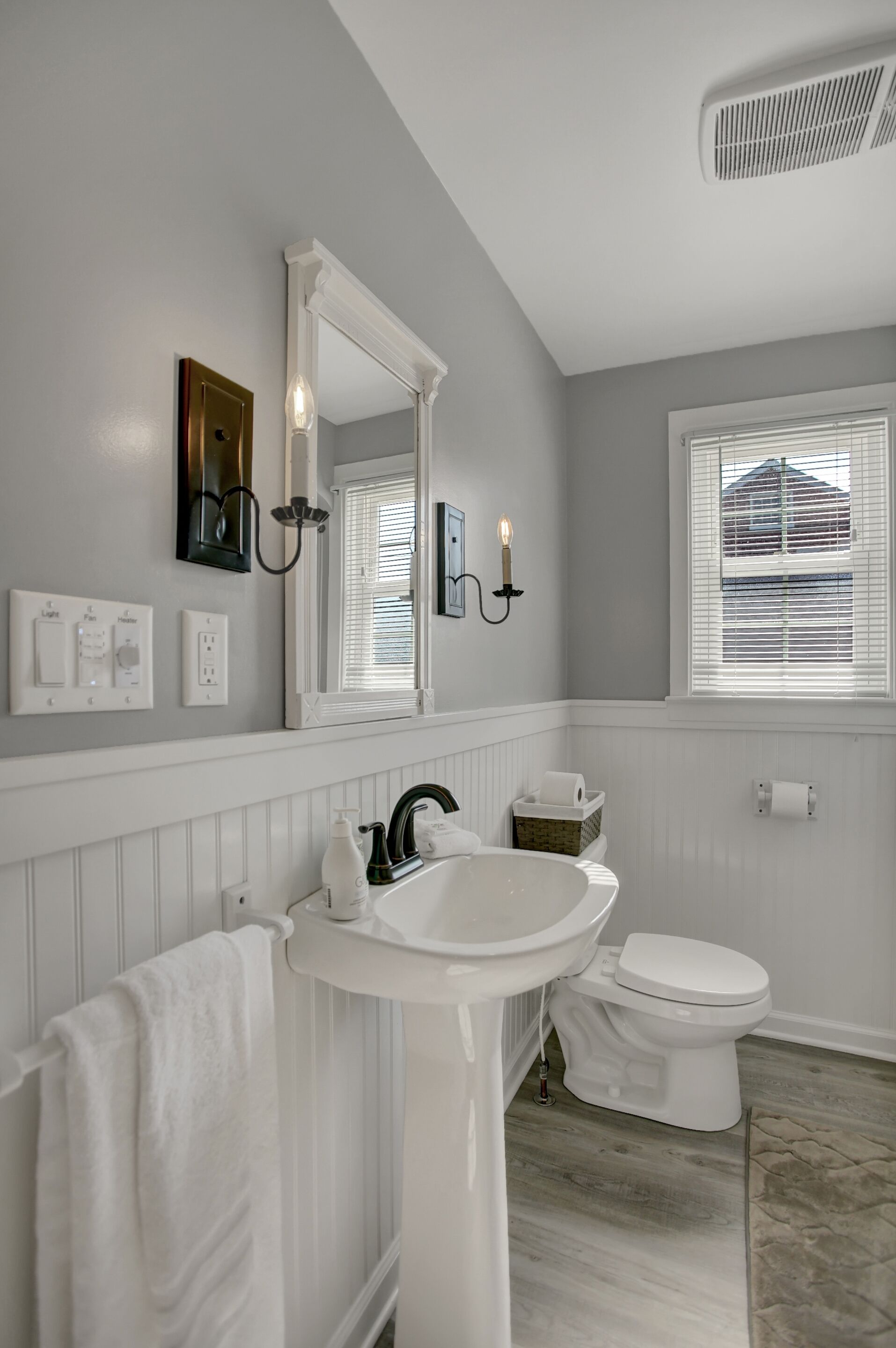 A bathroom with a white sink, vanity, and toilet. There is a mirror above the sink, and a window with blinds on the wall.