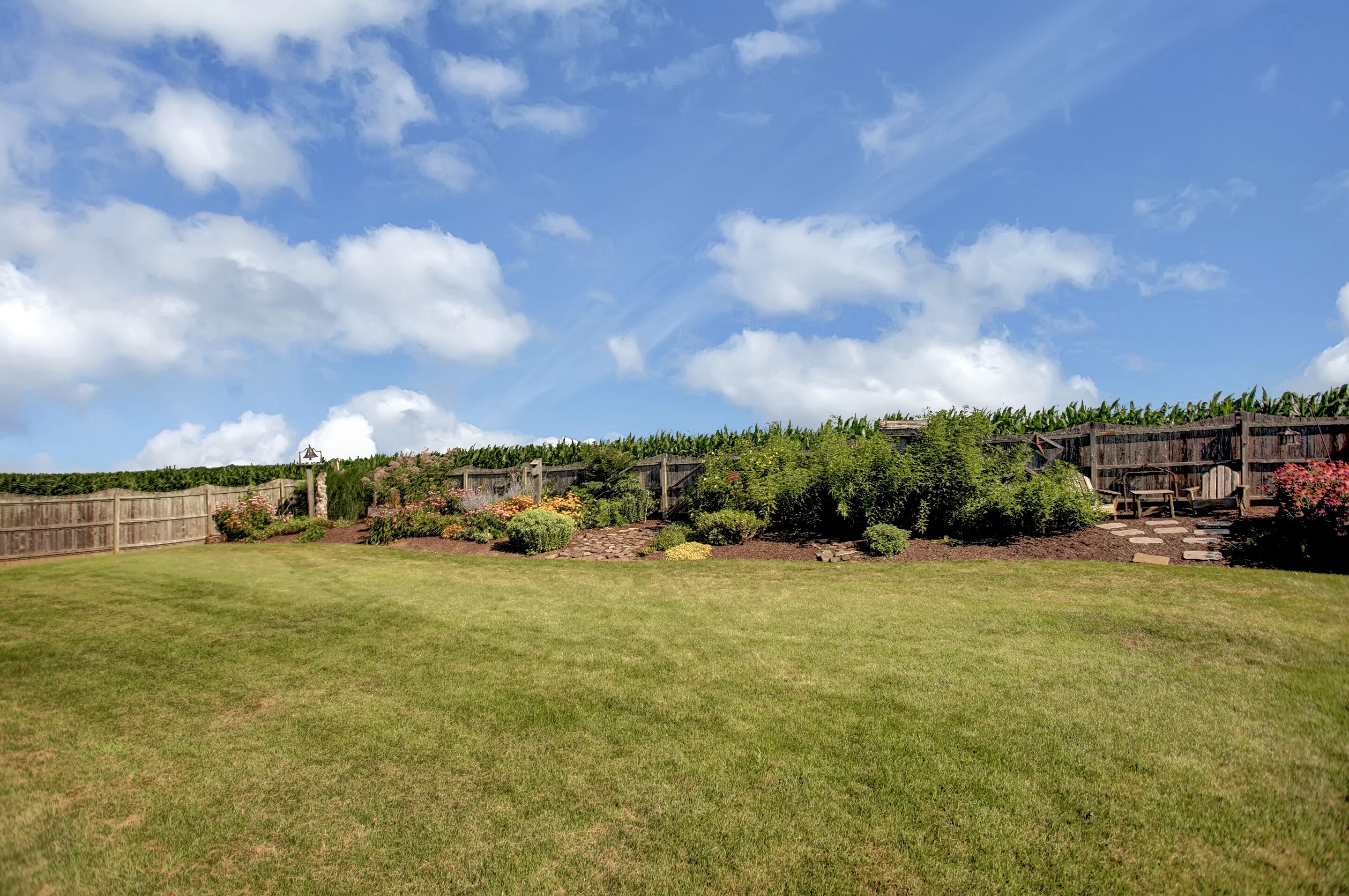 A spacious backyard with a wooden deck, a stone pathway, and various plants and flowers.