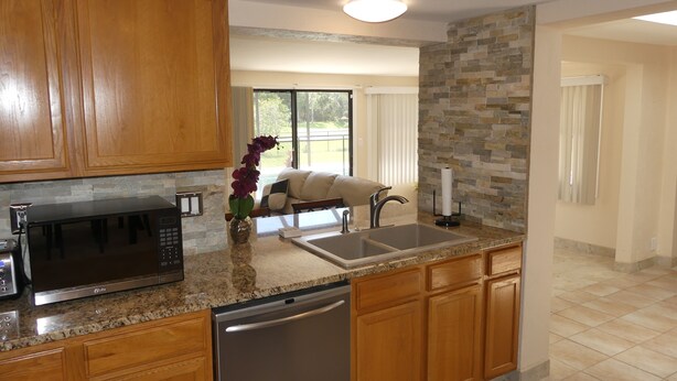 A modern kitchen with granite countertops, wooden cabinets, a built-in dishwasher, and a stone backsplash.