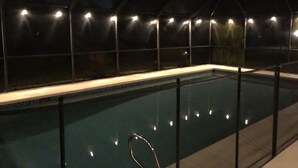 A swimming pool with a tiled edge and a metal ladder, surrounded by a dark, enclosed area with evenly spaced lights along the perimeter.