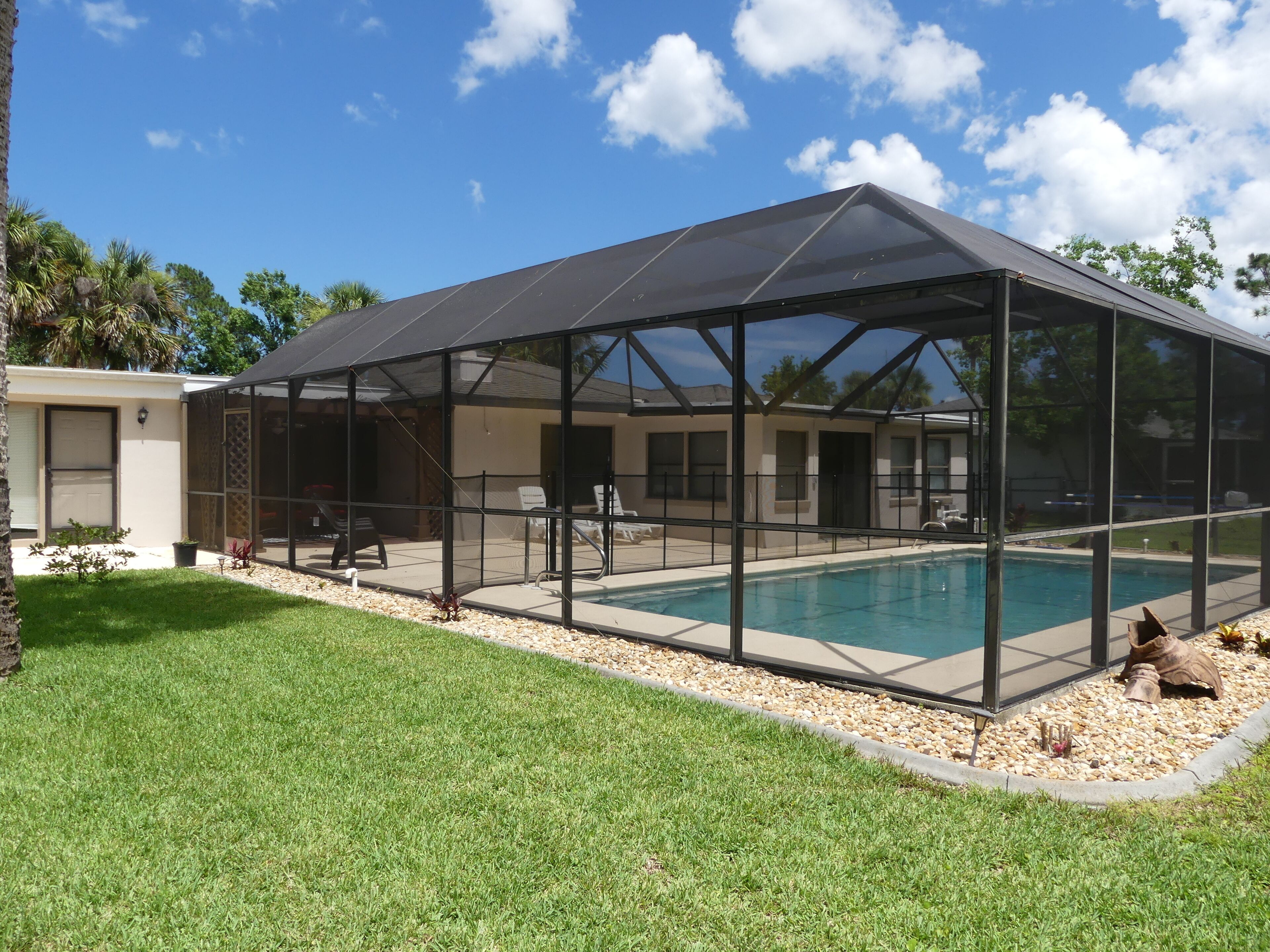 A covered outdoor swimming pool with a glass enclosure, surrounded by a grassy area and a small deck.