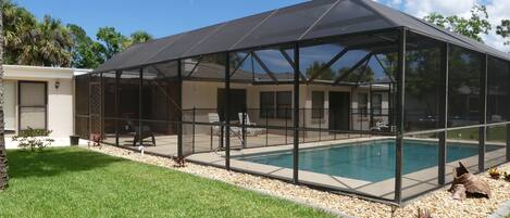 A covered outdoor swimming pool with a glass enclosure, surrounded by a grassy area and a small deck.