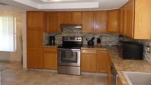 A kitchen with wooden cabinets, a stainless steel oven, a coffee maker, and a black refrigerator.